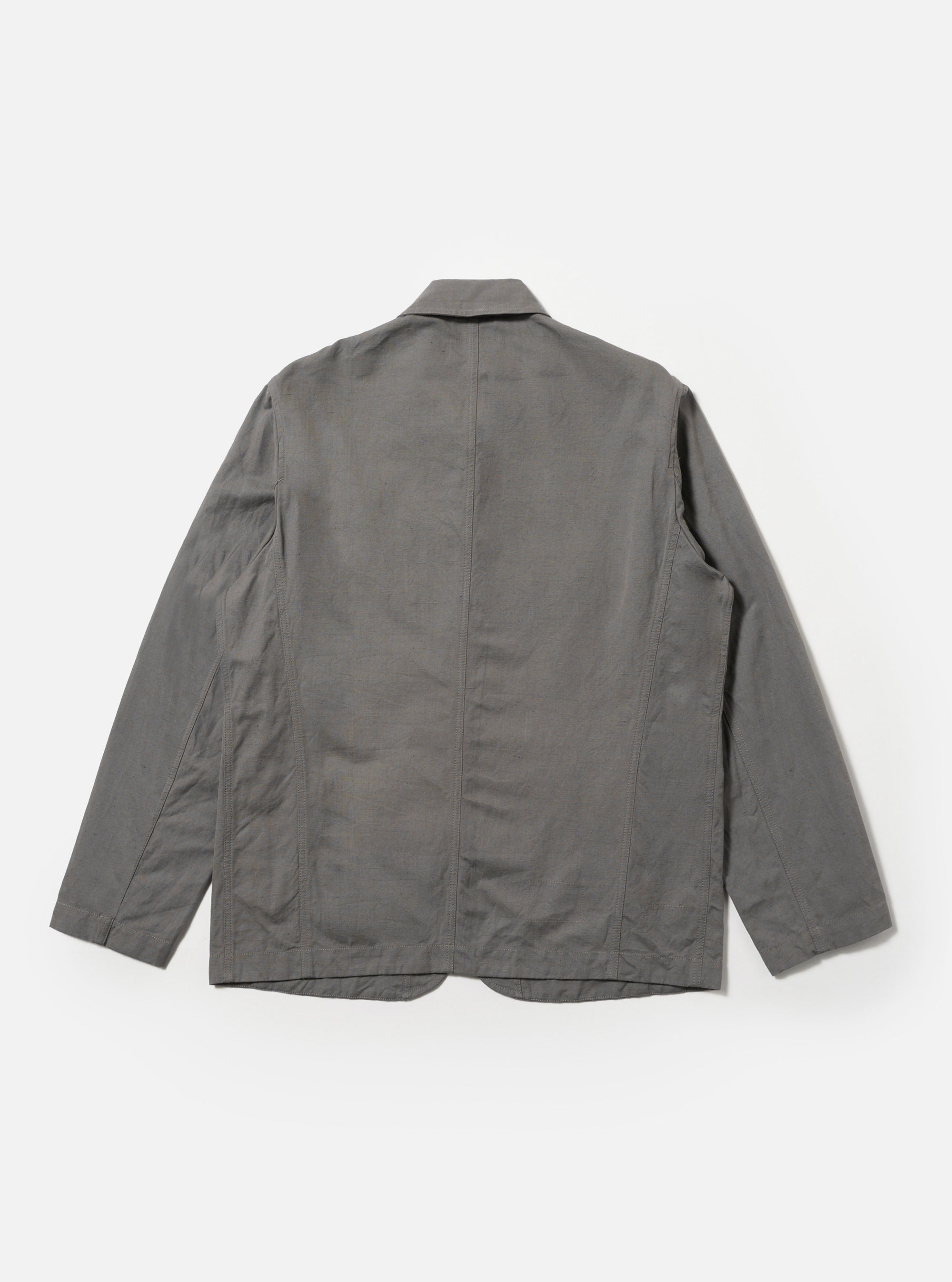 The Mid Grey Linen Slub Weave Bakers Jacket is shown from the back as a flat lay against a plain white background. The image highlights the jacket's simple construction, featuring a central vertical seam, a straight hem, and the textured appearance of the mid-grey linen-cotton blend fabric.