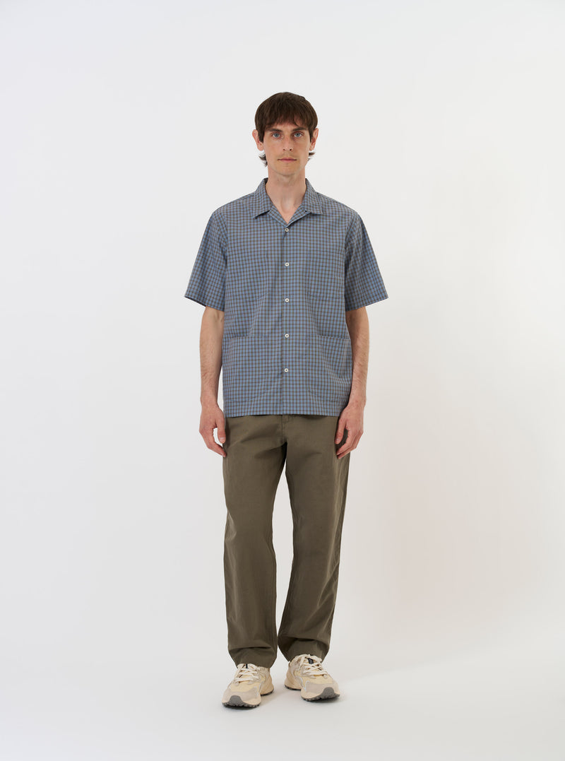 The Pale Blue Check Plaid Summer Overshirt is shown laid flat against a solid white background. The garment features a light blue and white plaid pattern, a classic pointed collar, a full button-down front, and two large chest pockets with buttoned flaps.