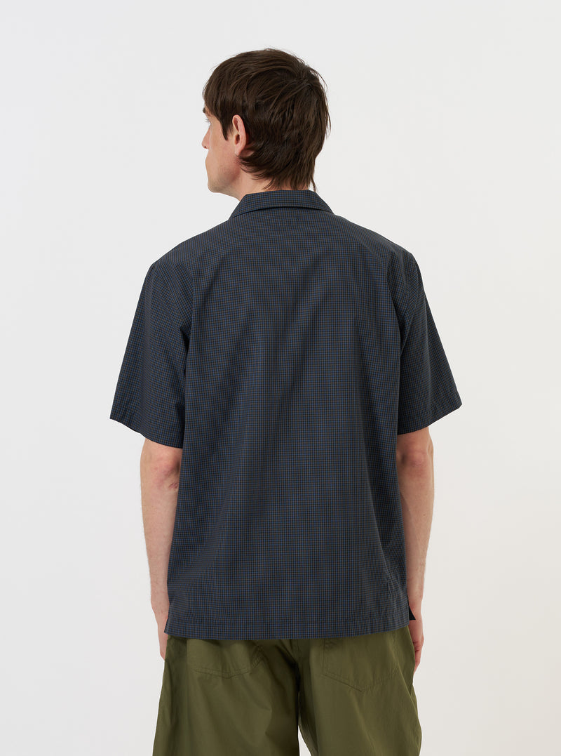 A model is wearing the Navy Check Plaid Summer Overshirt against a plain white background. The image, taken from a side-rear perspective, showcases the overshirt's dark navy and white plaid pattern and relaxed fit. The model is standing with their hands by their sides, highlighting the length of the sleeves and the garment's drape.