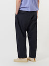 A model is wearing the Navy Broadcloth Oxford Pant against a plain white background. The image provides a view of the trousers from the waist down, showcasing the loose, wide fit and the deep navy blue color of the broadcloth fabric. The model is standing, and the trousers drape naturally, highlighting the pleated front and the textured finish of the material.