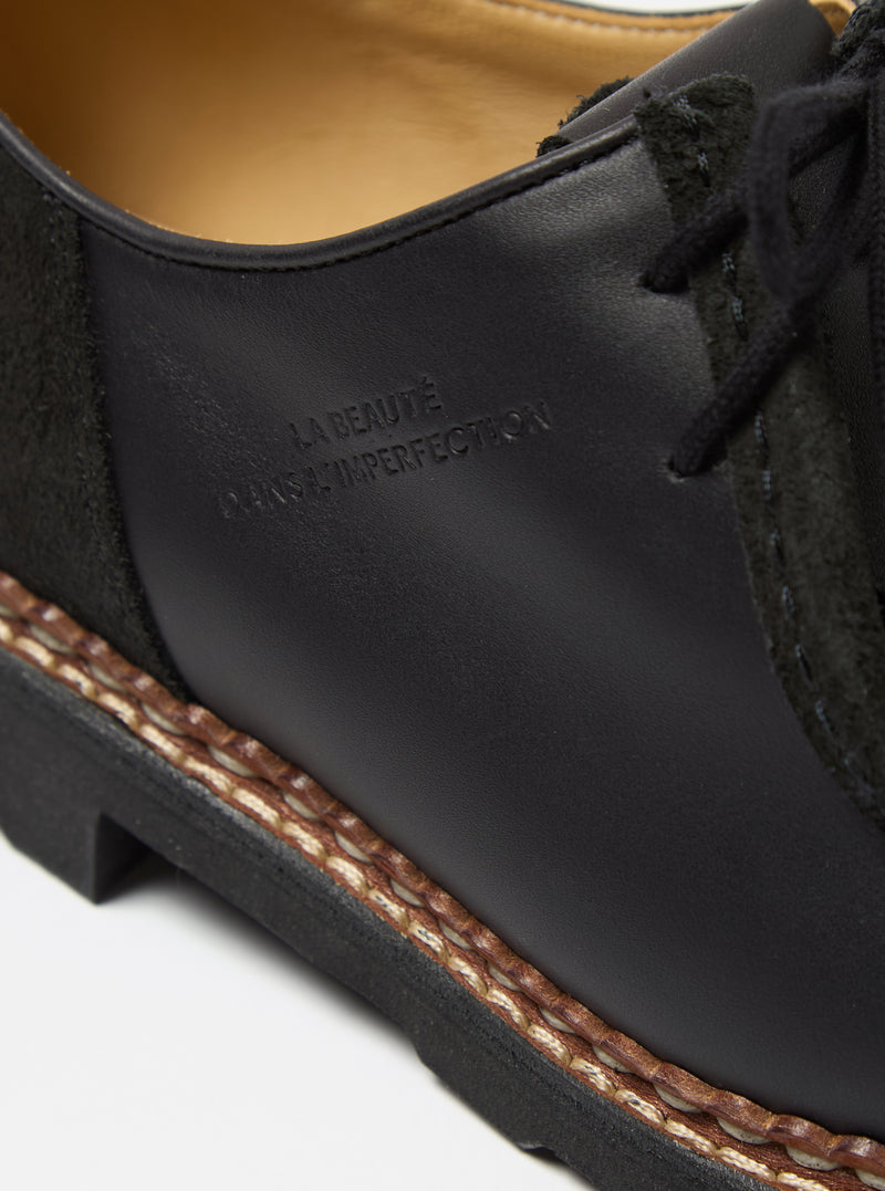 Close-up of the Paraboot x Universal Works Michael shoe in black leather and suede. Features include a welted sole and subtle branding. Shot on a clean white background.