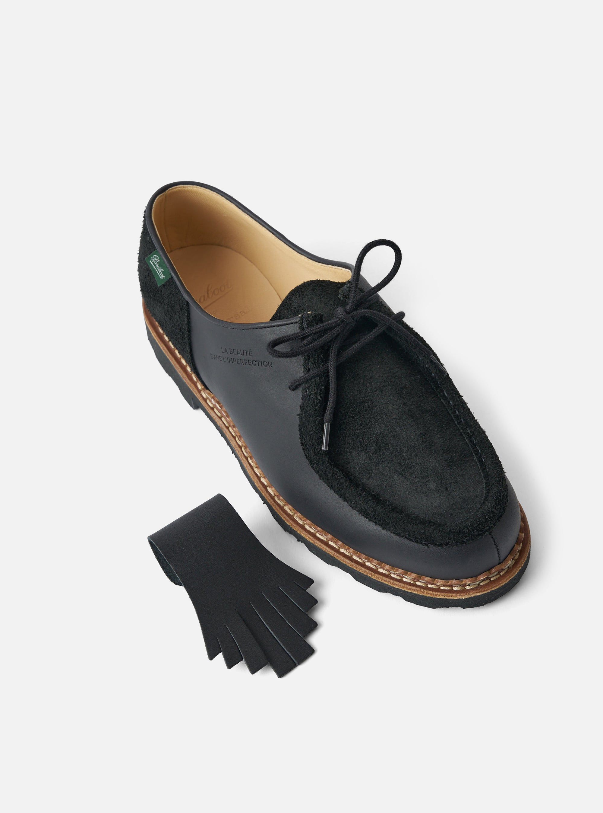 Studio shot of Paraboot x Universal Works Michael in Black Leather/Suede. The shoe is on a white surface with a leather tassel. The shoe features black leather and suede.