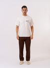 The Paraboot x Universal Works Ecru Single Jersey Print Tee is shown as a flat lay against a plain white background. This short-sleeve T-shirt features a ribbed crewneck and a large vintage-style graphic print on the front, depicting a character and co-branded detailing in dark ink. The ecru-colored cotton fabric has a smooth, single jersey texture.
