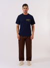 The Paraboot x Universal Works Navy Single Jersey Print Tee is shown as a flat lay against a white background. The short-sleeve t-shirt features a ribbed crewneck and a prominent white graphic print on the front inspired by vintage advertising. The garment is made from a solid navy blue cotton jersey.
