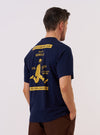 A model wears the Paraboot x Universal Works Navy Single Jersey Print Tee, shown from a rear angle against a plain white background. The image highlights a large graphic print on the back of the navy blue cotton shirt, which features a relaxed fit, short sleeves, and a ribbed crewneck.