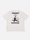 The Paraboot x Universal Works Ecru Single Jersey Print Tee is shown from the back as a flat lay against a plain white background. The image highlights a large dark graphic print centered on the upper back, featuring vintage-style typography and a central illustration. The t-shirt is made from a light ecru cotton fabric and features a simple straight hem and short sleeves.