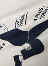 A close-up swatch image of the Paraboot x Universal Works Ecru Single Jersey Print Tee fabric highlights the soft ecru color and the fine, smooth texture of the single jersey cotton. The material fills the frame, showcasing the consistent weave of the garment.