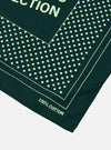 The Paraboot x Universal Works Green Cambric Neckerchief is displayed from the back as a flat lay against a plain white background. The image highlights the square shape of the accessory and the intricate dark-colored graphic print featuring collaboration branding and various illustrated motifs on the green cotton fabric.