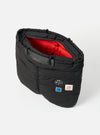 The Topologie x Universal Works Black UW Tech Helmet Bag, open to show the red interior. Patches adorn the black exterior. Shot against a white backdrop.