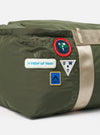 Close-up of the Topologie x Universal Works Rifle Green UW Tech Summit Duffle Large. Features patches, beige strap, and embossed logos on a green material. Shot on a white background.