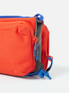 Close-up of the Topologie x Universal Works Red UW Tech Bottle Sacoche Medium. It features a red body, blue trim, and gray interior, set against a clean white backdrop.