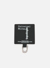 Close-up of the Topologie x Universal Works Black UW Tech Phone Strap Adapter on a white background. The black fabric adapter features white text and a silver metal loop.