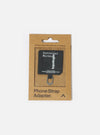 Topologie x Universal Works Black UW Tech Phone Strap Adapter in its brown cardboard packaging. The adapter is black with silver hardware, on a white background.