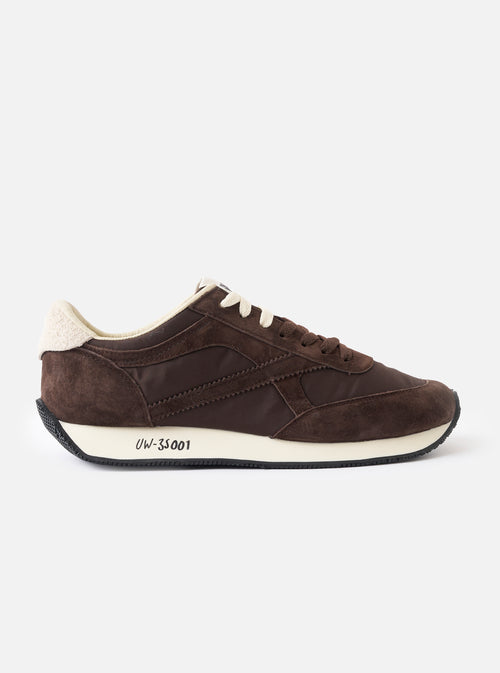 A side profile view of the Walsh x Universal Works Tornado sneaker in brown leather and canvas set against a clean white background, showcasing the suede panelling, layered upper construction, white midsole, and Vibram lugged outer sole.