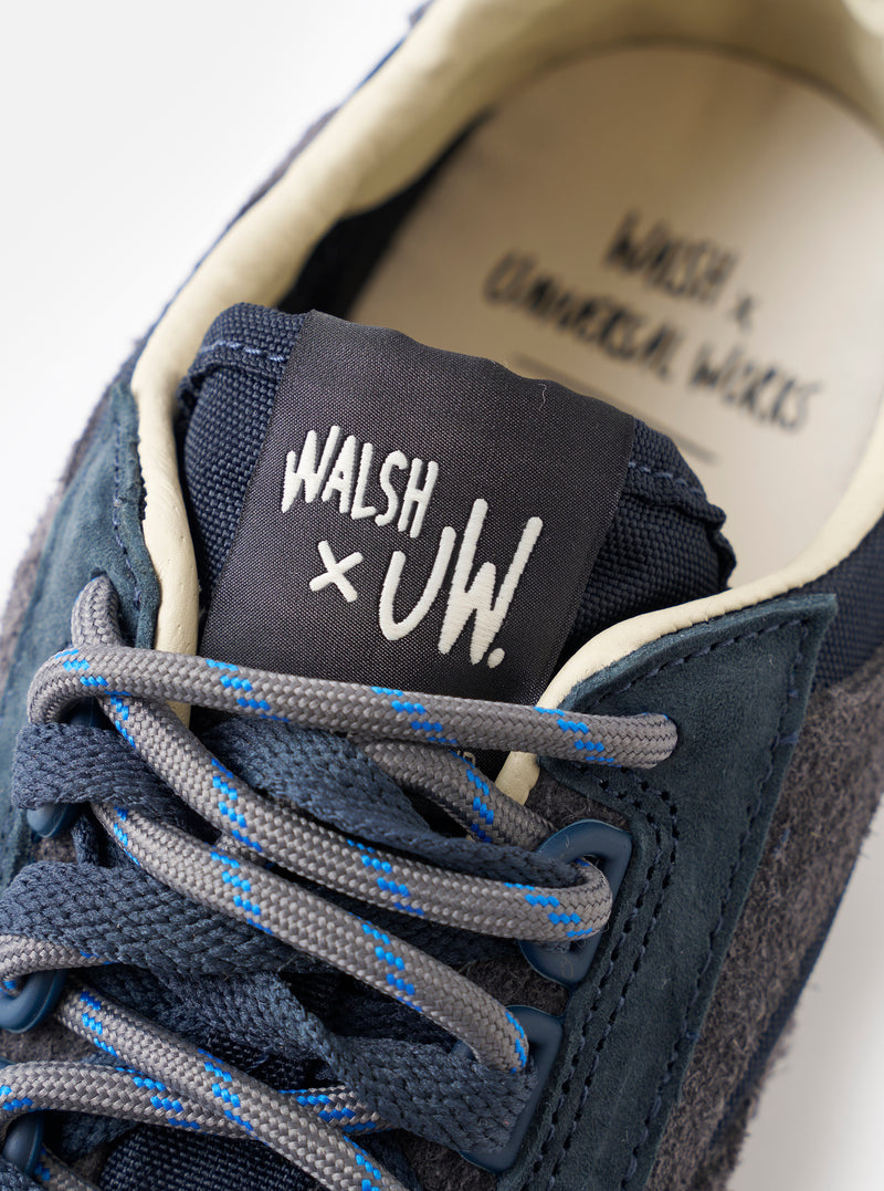 An angled view of the sole of the Walsh x Universal Works Ensign in Navy Leather/Canvas sneaker presented against a plain white background, illustrating the deep tread pattern and rugged rubber outsole design.
