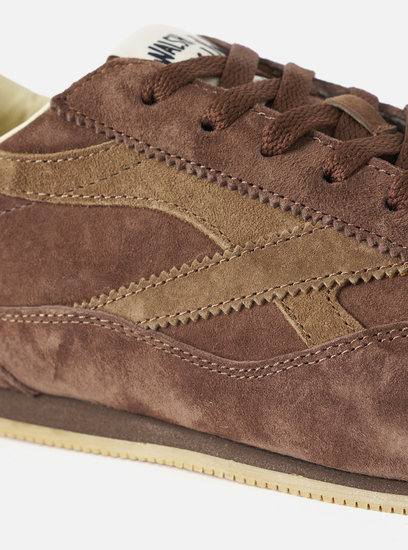A top-down aerial view of the Walsh x Universal Works Cob in Brown Leather trainer against a plain white background, detailing the symmetry of the lace placket, soft leather lining, and minimalist internal branding.