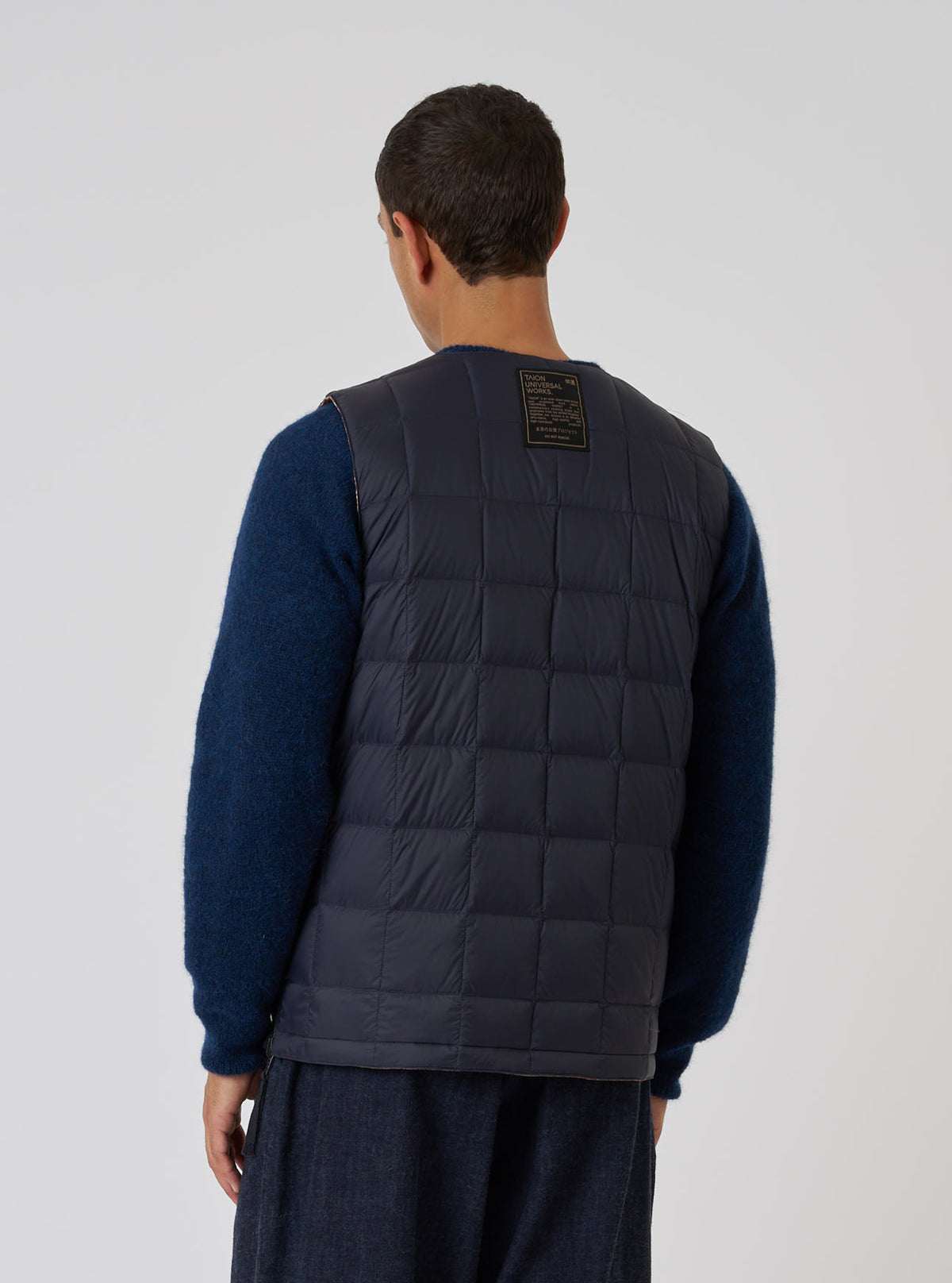 Back view of a model wearing the TAION x Universal Works Reversible Dark Navy Military Line Vest. The vest is quilted and dark navy. Shot against a white backdrop.