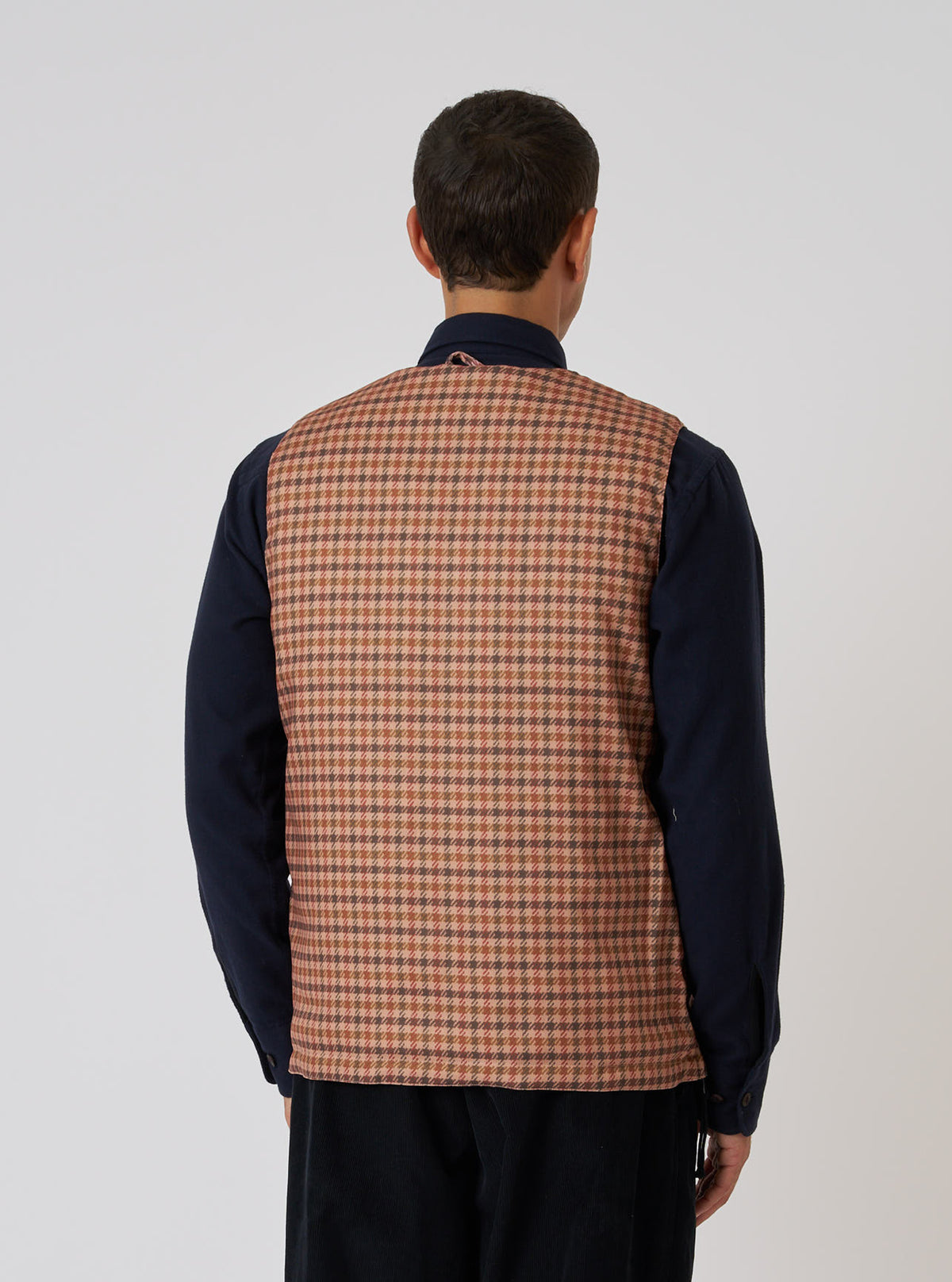 Back view of a model wearing the TAION x Universal Works Reversible Dark Olive Military Line Vest. The vest has a brown and beige houndstooth pattern. Shot on a white background.