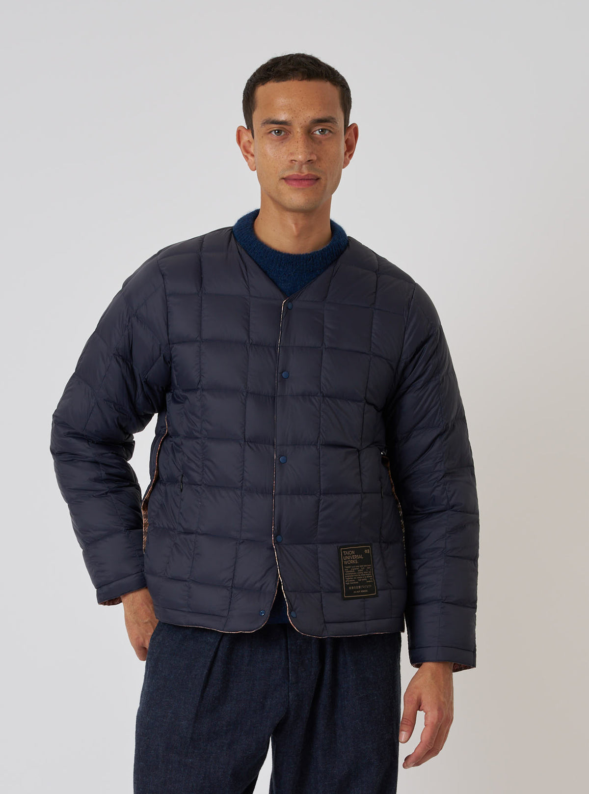 A model wears the TAION x Universal Works Reversible Dark Navy Military Line Liner Jacket. The quilted jacket is styled in front of a plain white backdrop.