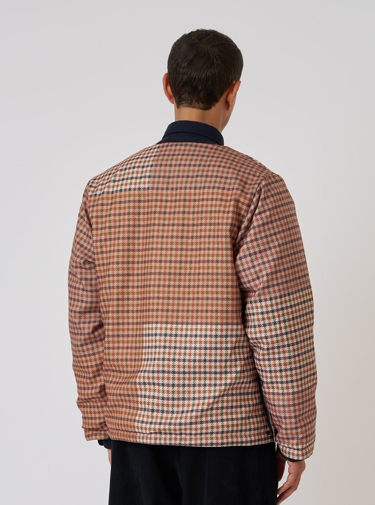 Back view of a model wearing the TAION x Universal Works Reversible Dark Olive Military Line Liner Jacket. The jacket is a brown and tan houndstooth pattern. Shot on a white background.