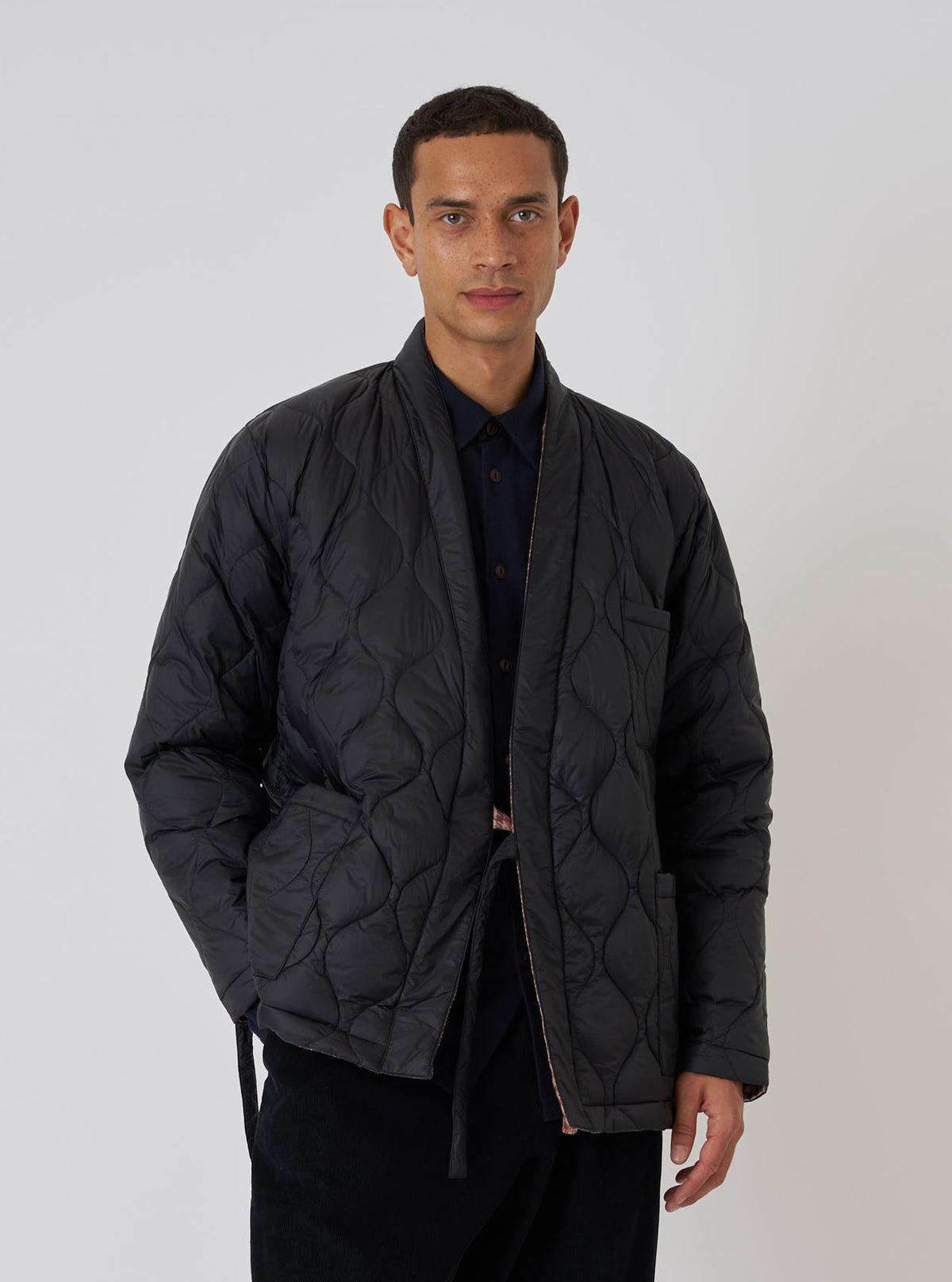 A model poses in a TAION x Universal Works Reversible Black Military Line Kyoto Work Jacket. The quilted jacket is styled in front of a plain white background.