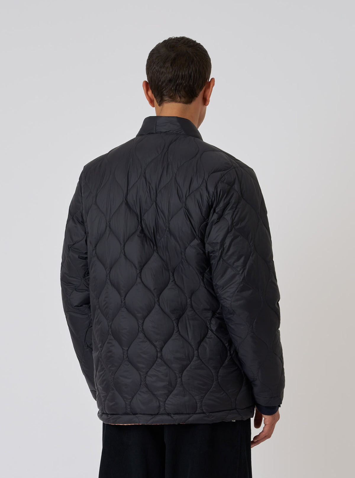 Back view of a model wearing the TAION x Universal Works Reversible Black Military Line Kyoto Work Jacket. Quilted design, against a plain white backdrop.