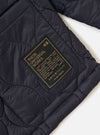 Close-up of the TAION x Universal Works Reversible Dark Navy Military Line Kyoto Work Jacket showing the quilted texture and branded patch on a white background.