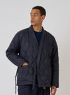 A model wears the TAION x Universal Works Reversible Dark Navy Military Line Kyoto Work Jacket. The quilted jacket has a tie waist and is set against a plain background.