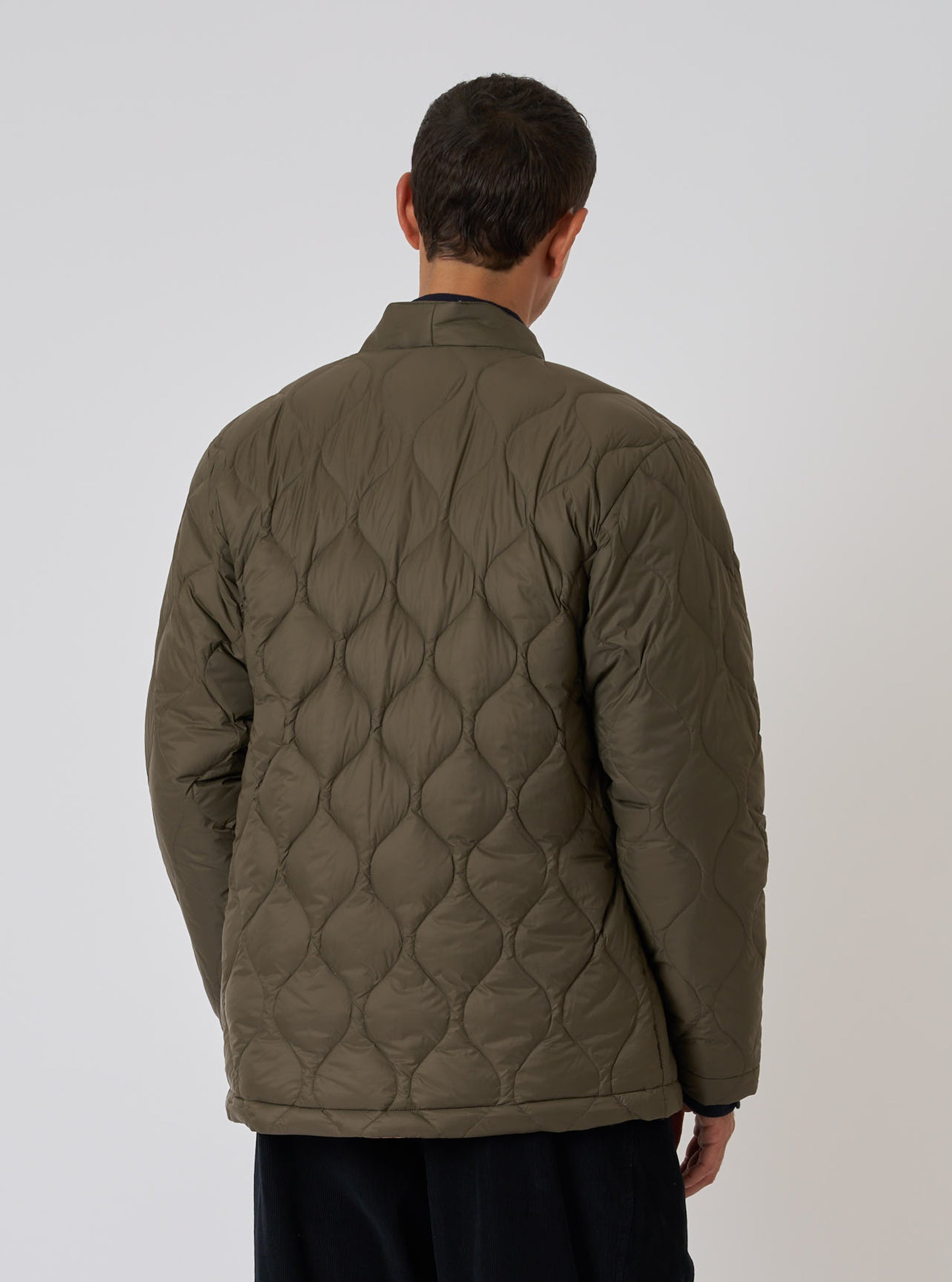 Back view of a model wearing the TAION x Universal Works Reversible Dark Olive Military Line Kyoto Work Jacket. The quilted jacket is displayed against a plain white background.