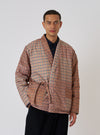 A man poses in front of a white backdrop, wearing the TAION x Universal Works Reversible Dark Navy Military Line Kyoto Work Jacket. The jacket features a brown and tan houndstooth pattern.