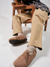 Person sitting in a chair wearing Malibu Walnut/Tan Vegan Leather/Crepe Latigo shoes. The shoes are tan and brown, and the person is wearing tan pants and socks. White background.