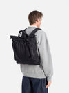 Back view of a model wearing the F/CE.® Black Recycled Twill 3-Way Helmet Bag as a backpack. The bag is black and made of twill. The background is a clean white studio.