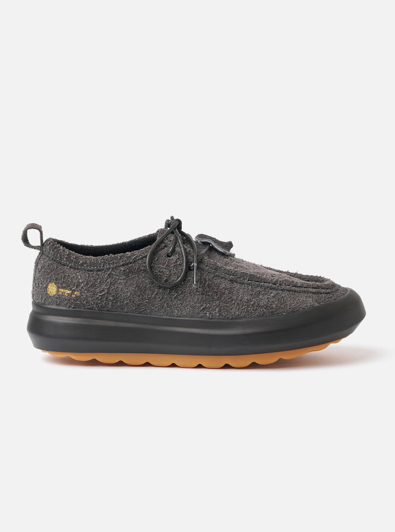 The Wander etc. FD/08 Low in Black Asphalt/Gum Hairy Suede is shown in a studio shot against a plain white background. The shoe features a black hairy suede upper with a low-cut silhouette, slim black laces, and a prominent chunky gum rubber sole. The textured finish of the suede and the contrast between the black upper and the tan-colored sole are clearly visible.