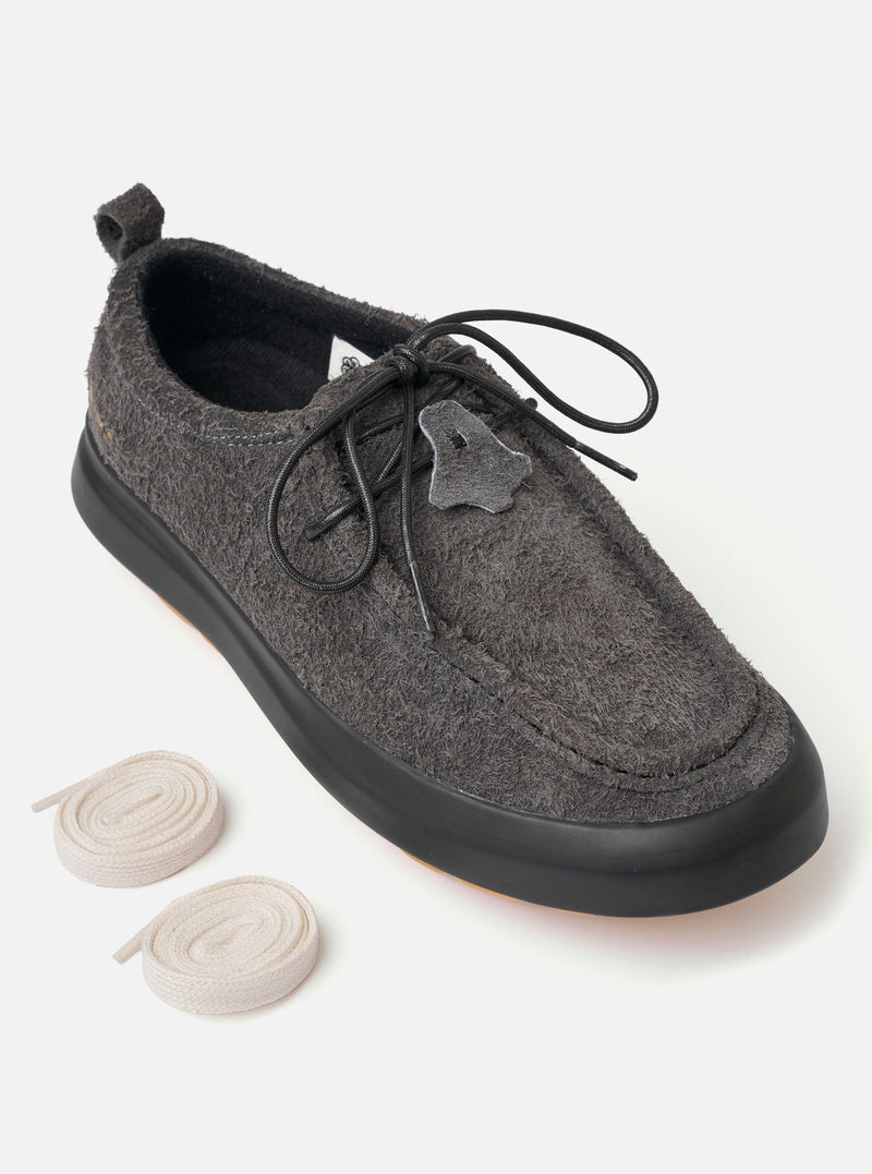 The Wander etc. FD/08 Low in Black Asphalt/Gum Hairy Suede is shown from a side profile as a flat lay against a plain white background. The shoe features a black hairy suede upper, slim black laces, and a chunky gum rubber outsole. The low-cut design and textured leather are the prominent features.