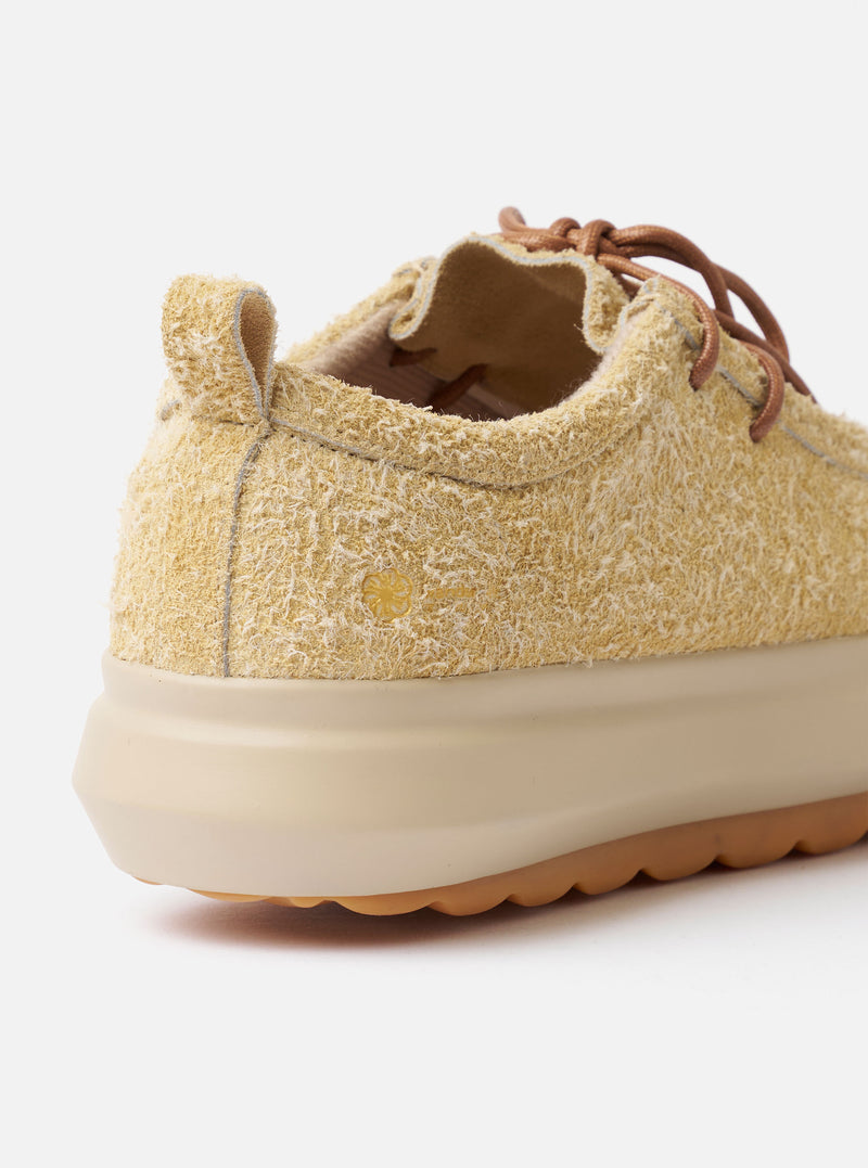 The Wander etc. FD/08 Low in Dune/Gum Hairy Suede is shown from a rear angle as a flat lay against a plain white background. The image highlights the shoe's heel, featuring a pull tab and branding, along with the thick gum-colored rubber outsole. The textured dune-colored hairy suede upper and the chunky laces are also prominent.