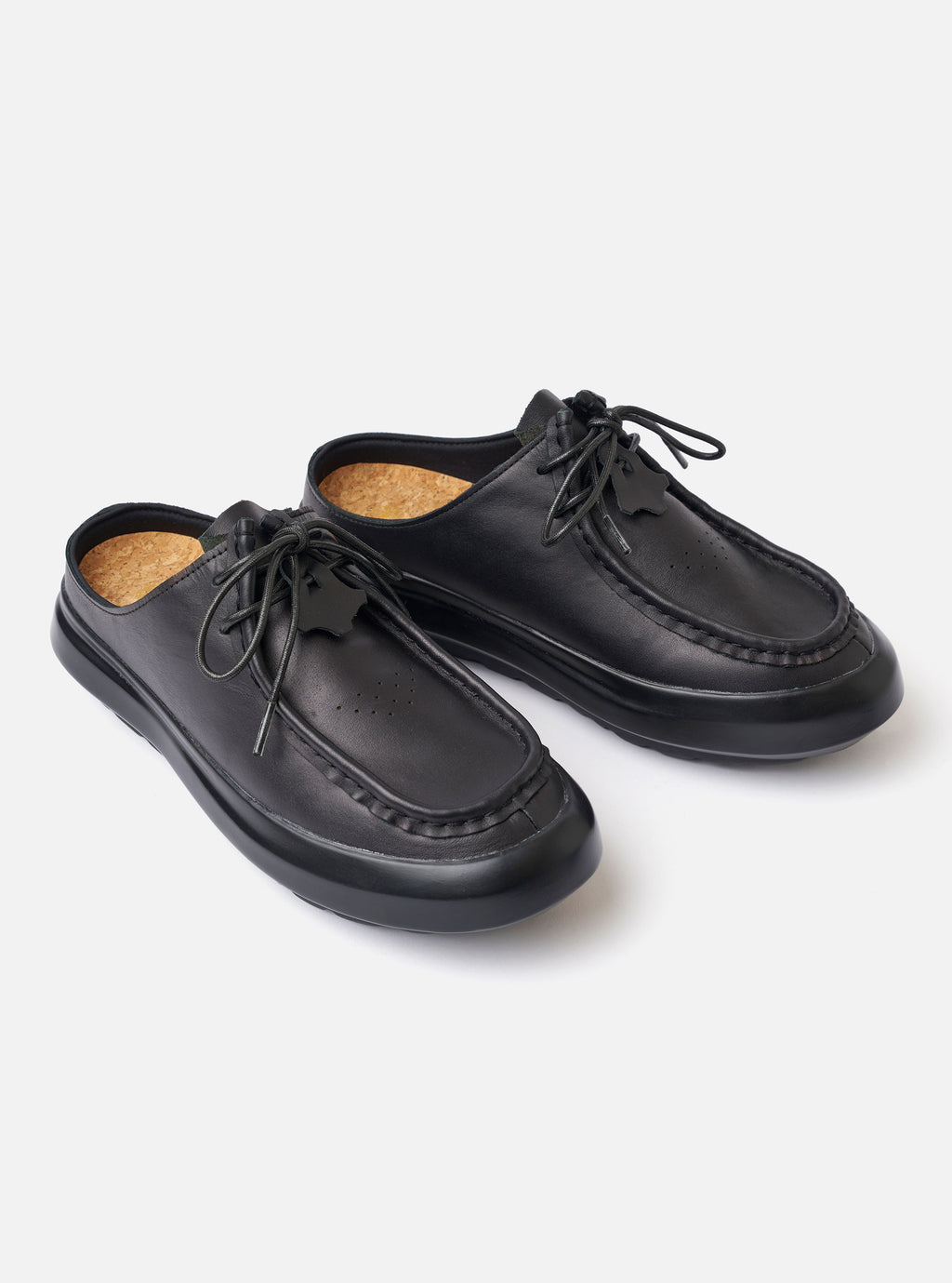 The Wander etc. Laze in Black Nappa Leather is shown in a detail view as a flat lay against a plain white background. The image highlights the backless mule design, featuring a smooth black nappa leather upper and a chunky phylon and gum outsole with a cork footbed.