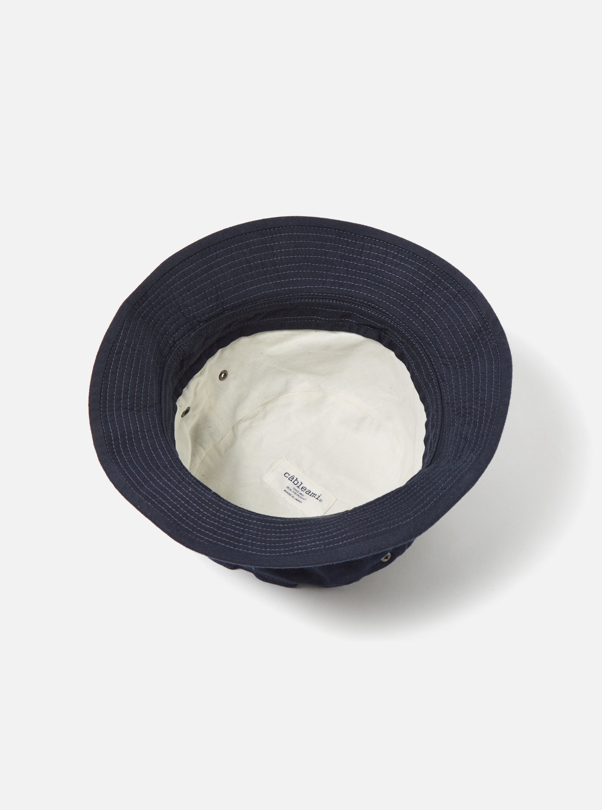 Close-up of the inside of a cableami® Navy Chino Cotton Loose Light Pork Pie Hat on a white background. Shows the light-colored lining and brand label.