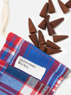 Harvest Incense Cones - Eucalyptus, Fir Needle & Patchouli - 20 pack, scattered on a white surface next to a red, white, and blue plaid bag with a white drawstring.