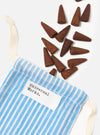 Harvest Incense Cones - Eucalyptus, Fir Needle & Patchouli - 20 pack, displayed on a white surface next to a blue and white striped bag. The cones are brown and cone-shaped.