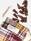 Harvest Incense Cones - Eucalyptus, Fir Needle & Patchouli - 20 pack. Brown incense cones spill from a colorful plaid bag with a white drawstring on a white surface.
