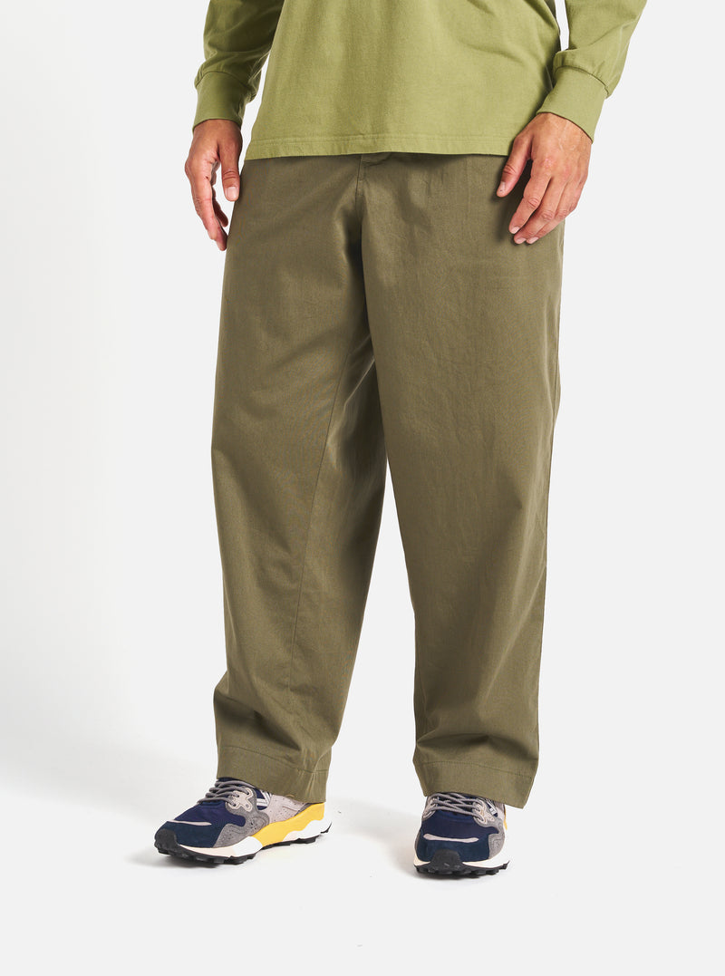 A model stands against a white backdrop, showcasing the Light Olive Twill Duke Pant. The pants are paired with a matching light olive shirt and colorful sneakers.