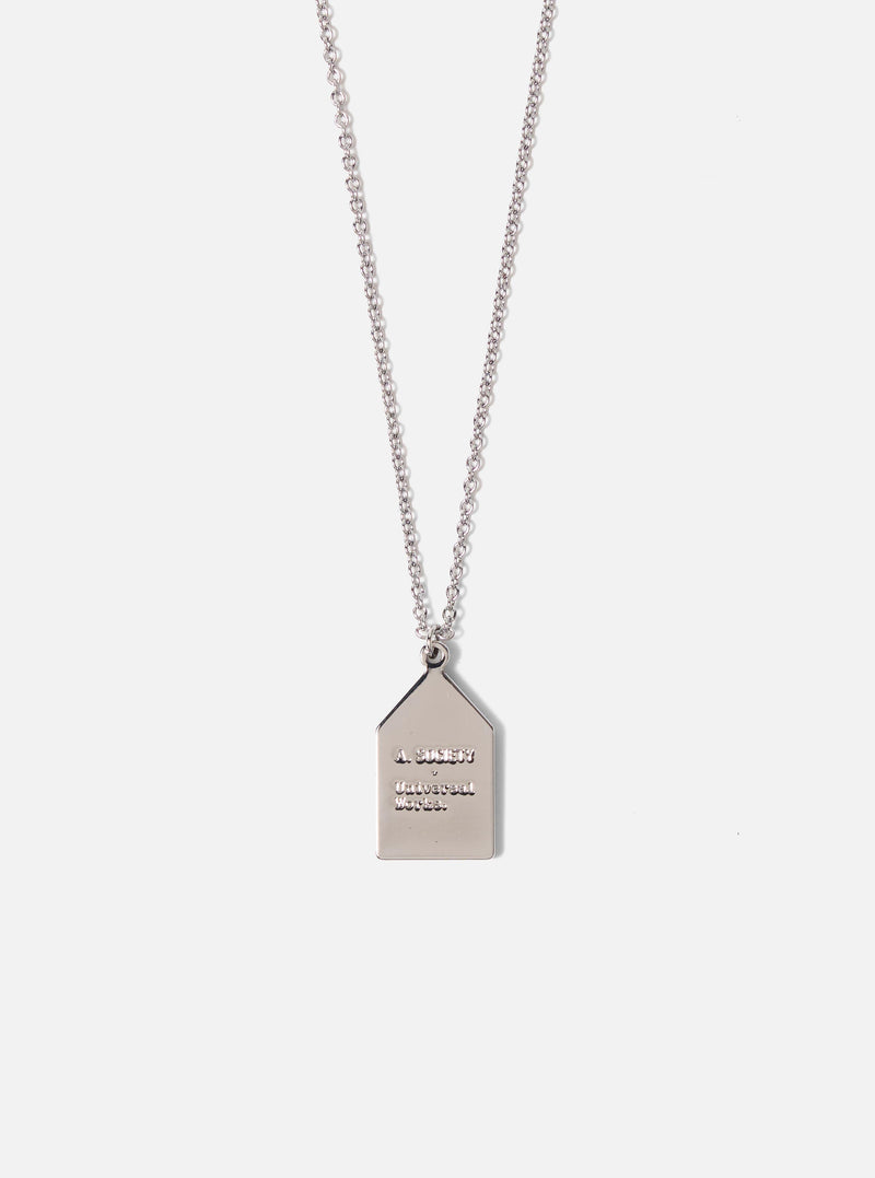 Close-up of the A. SOCIETY x Universal Works Brown Necklace on a white background. The silver pendant has the brand names engraved.