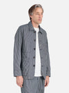 A man models the Indigo Hickory Stripe Denim Original Bakers Jacket against a white backdrop. The jacket features a striped pattern and button closure.