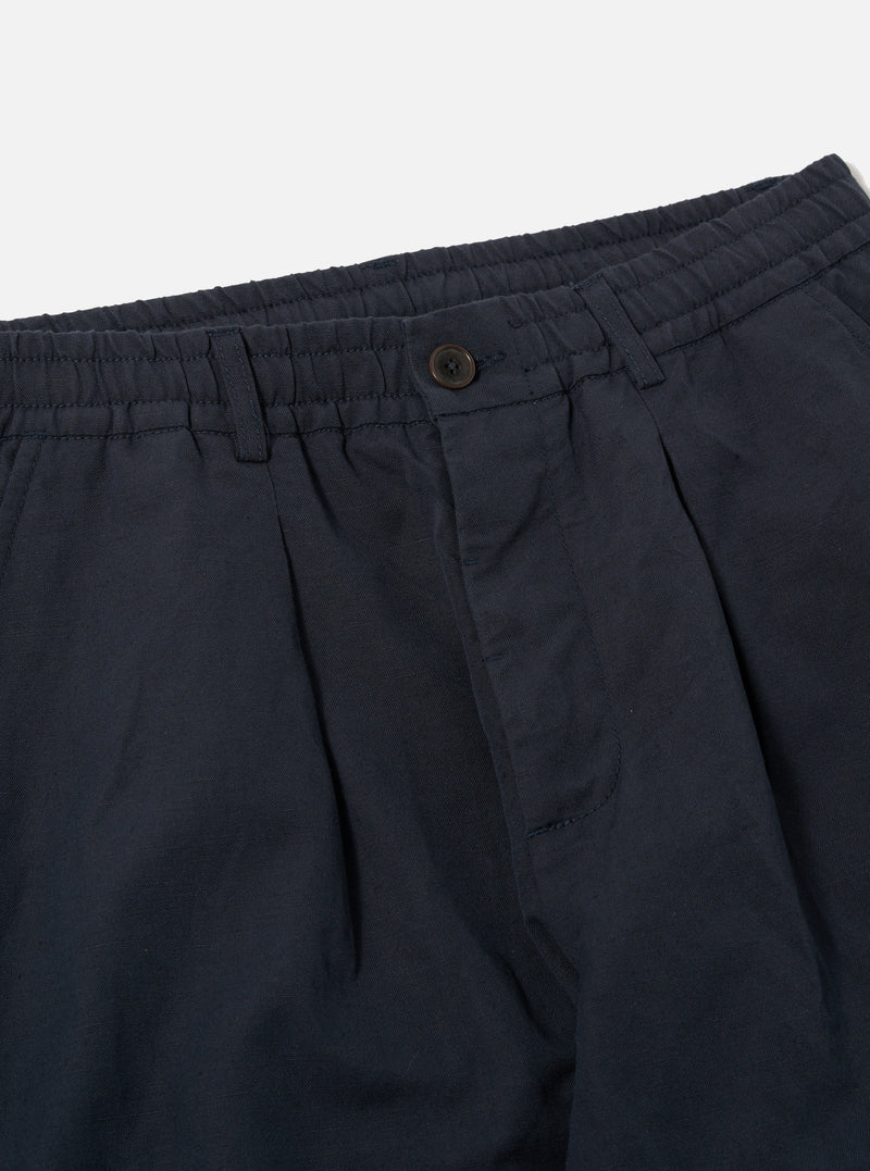 Close-up of the Navy Linen Slub Weave Oxford Pant on a white background. Shows the navy color, linen texture, button closure, and pleated design.
