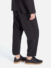 Side view of a model wearing Charcoal Fine Linen Mix Pleated Track Pant. The pants are paired with black sneakers. The background is a clean, bright white.