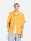 A model on a white background wears the Mustard Dobby Self Stripe Camper Shirt. The shirt is mustard-colored with a dobby self stripe pattern. The model also wears light blue pants.