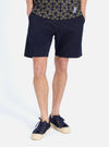 A model wears the Navy Military Cotton Simple Short on a white background. The cotton shorts are paired with navy sneakers and a patterned shirt.