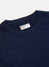 Close-up of the Navy Single Jersey Print Pocket Tee on a white surface. The navy tee shows the collar and a tag that says "Universal Works."