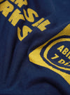Close-up of the Navy/Yellow Single Jersey Print Pocket Tee, showing the fabric texture and yellow print on the navy material. 