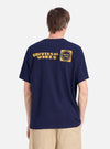 Back view of a model wearing a Navy/Yellow Single Jersey Print Pocket Tee. The tee has yellow print on the back. The background is a plain white studio backdrop.
